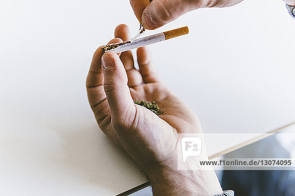 Abgetrennte Hand eines Mannes  der Marihuana-Gelenke hält  während er am Tisch eine Zigarette zerreißt