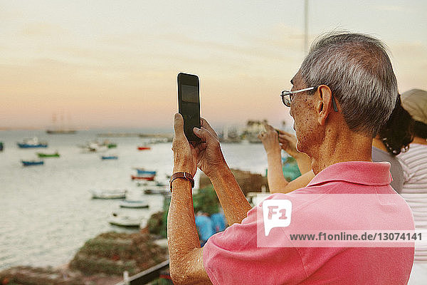 Älterer Mann fotografiert mit einem Smartphone  während er mit seinen Geschwistern am Hafen steht