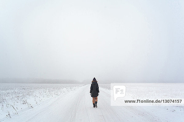Rückansicht einer Frau  die bei nebligem Wetter auf einem verschneiten Feld gegen den Himmel läuft