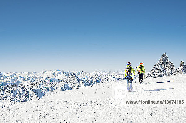Rückansicht von Wanderern  die auf einem schneebedeckten Berg bei strahlend blauem Himmel wandern