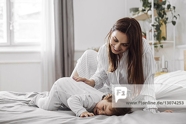 Happy woman playing with baby boy in bed at home
