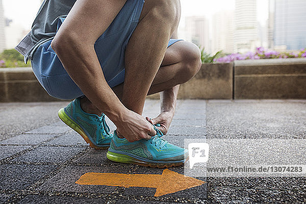 Low section of man tying shoe lace while kneeling by arrow symbol on floor