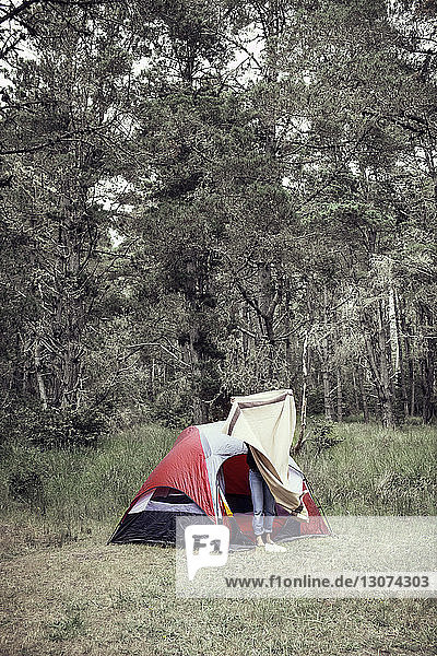 Frau mit Decke vor Zelt an Bäumen stehend