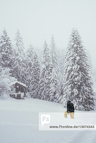 Rückansicht einer Frau  die bei Schneefall auf einem schneebedeckten Berg läuft