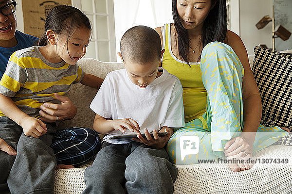 Familie sieht Jungen am Tablet-Computer an  während er zu Hause auf dem Sofa sitzt