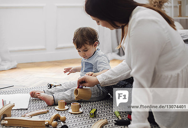 Baby boy looking at mother pouring tea in toy teacup at home
