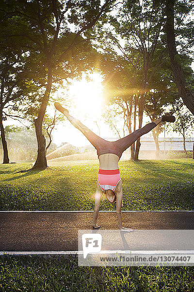 Woman performing handstand on road against trees in sunny day