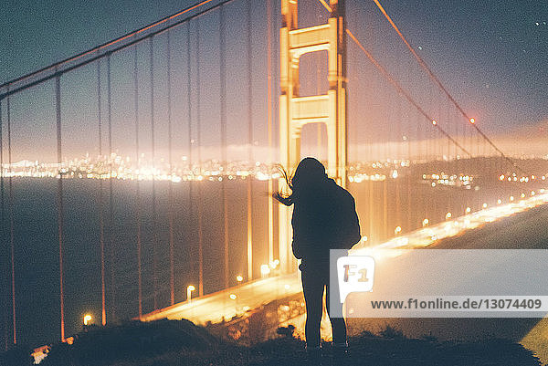 Silhouettenfrau steht nachts vor der beleuchteten Golden Gate Bridge