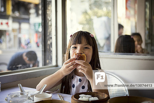 Portrait of girl holding bun while sitting in restaurant