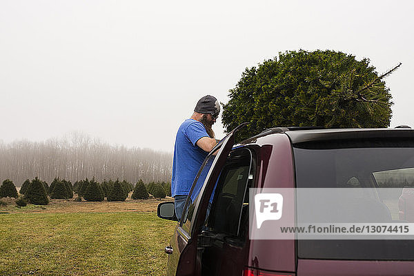 Side view of man standing by car on grassy field against clear sky