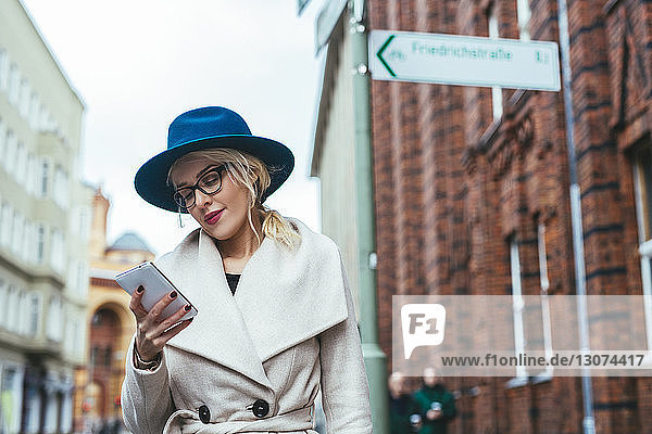 Niedriger Blickwinkel einer Frau  die ein Mobiltelefon benutzt  während sie auf einer Straße in der Stadt steht