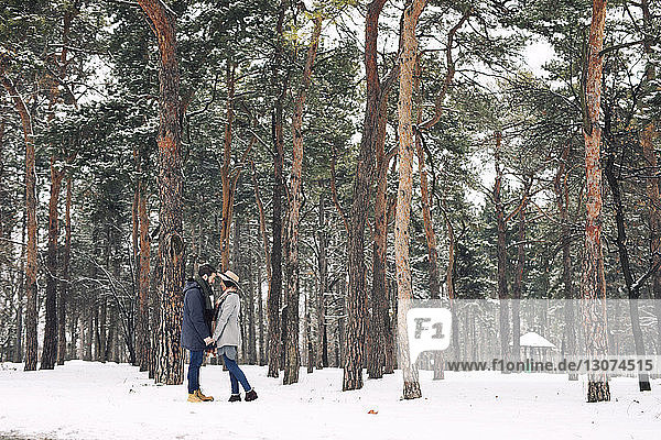 Happy couple looking at each other while standing on snowy field in forest