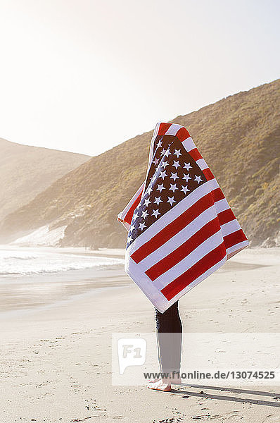 Frau in amerikanische Flagge gehüllt  die auf Sand vor klarem Himmel steht