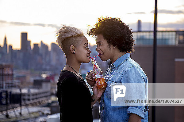 Couple drinking from bottle on rooftop during sunset
