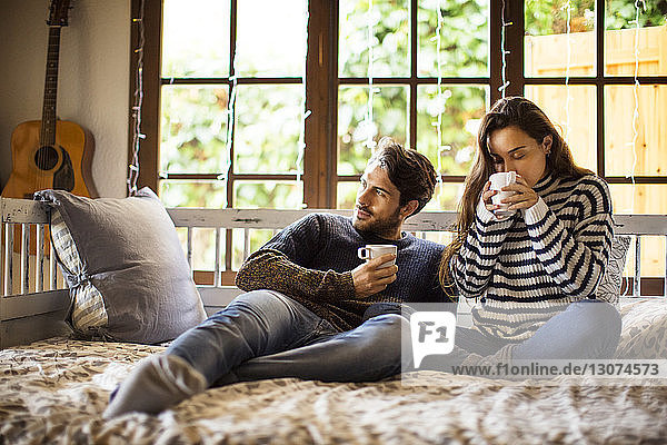 Ehepaar trinkt Kaffee  während es zu Hause auf einem Fensterplatz in einer Nische sitzt