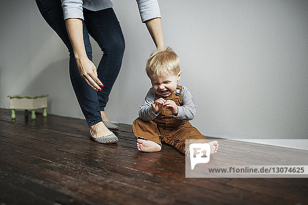 Low section of mother standing by cheerful baby boy sitting on floor at home