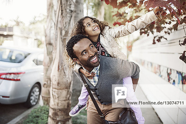 Mädchen zupft Blatt  während der Vater auf dem Fußweg Huckepack reitet