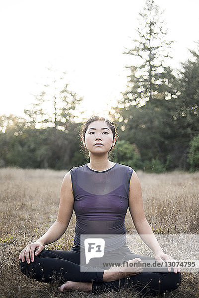 Porträt einer selbstbewussten Frau mit gekreuzten Beinen  die auf dem Feld Yoga praktiziert
