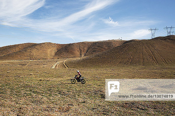 Mitteldistanzansicht einer Motorrad fahrenden Frau auf Landschaft gegen Himmel
