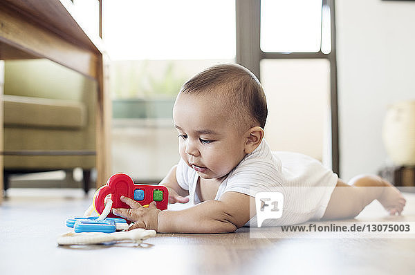 Kleiner Junge spielt mit Spielzeug  während er zu Hause auf dem Boden liegt