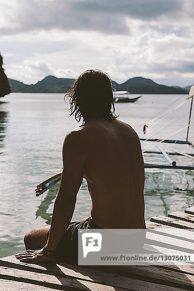 Thoughtful shirtless man sitting on jetty over sea