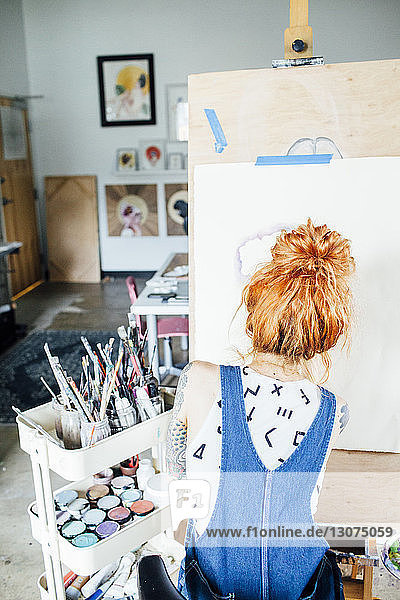 Rückansicht der Künstlerin  die im Atelier eine Skizze auf Leinwand zeichnet