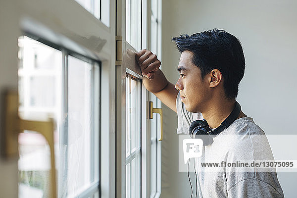 Thoughtful businessman looking through window while standing in office