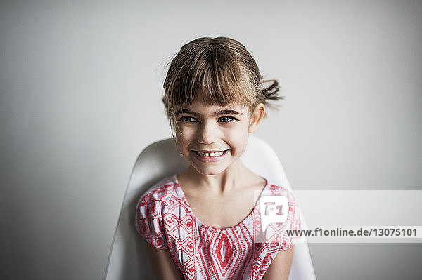Cheerful girl looking away while sitting on chair at home