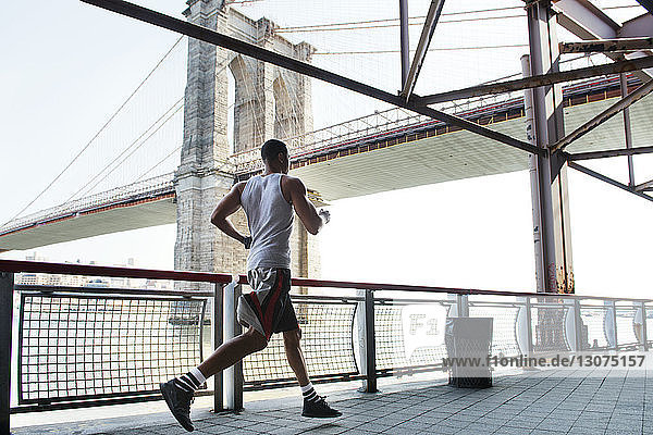 Rückansicht eines Mannes  der am Geländer gegen die Brooklyn Bridge rennt