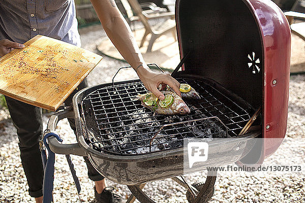 Midsection of man grilling fish on barbecue at yard