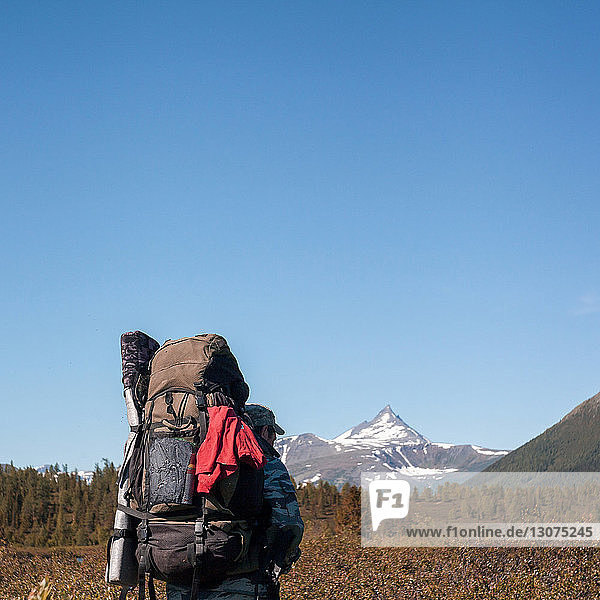 Rückansicht eines Wanderers mit Rucksack beim Wandern in der Landschaft vor klarem Himmel im Winter