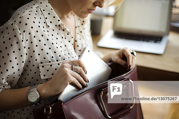 Mittelsektion einer Frau  die einen Tablet-Computer in die Handtasche im Heimbüro steckt