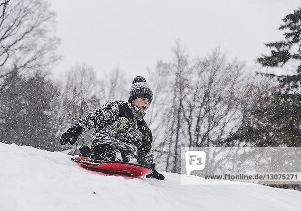 Boy sitting on sled while tobogganing on snow during snowfall