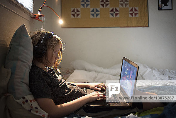Seitenansicht eines Jungen  der einen Laptop benutzt  während er zu Hause auf dem Bett sitzt