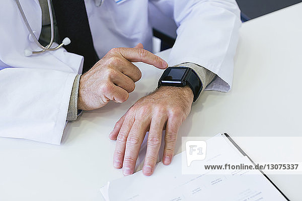 Beschnittenes Bild eines Arztes mit einer intelligenten Uhr am Tisch im Krankenhaus
