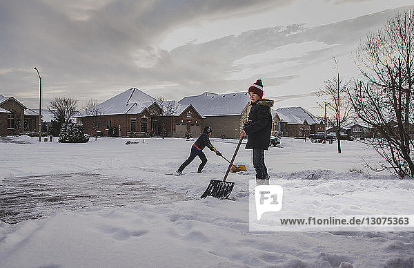 Brüder  die Schnee auf der Straße gegen Häuser schaufeln