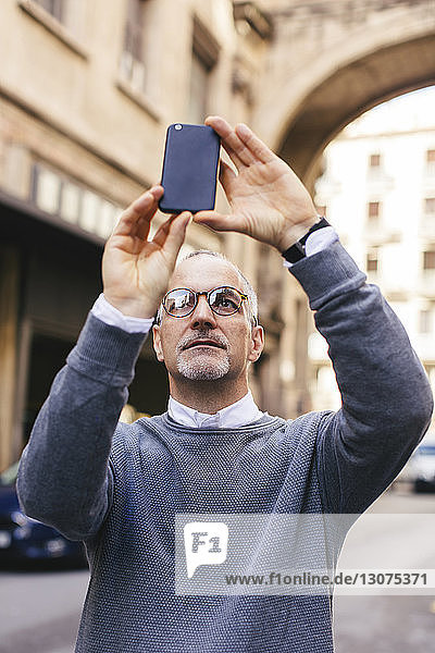 Man photographing with smart phone while standing in city