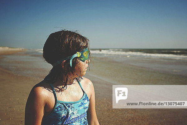 Girl wearing swimming goggles while looking at sea on St. Augustine Beach during sunny day