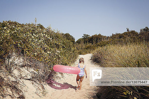 Rückansicht eines Mädchens  das einen aufblasbaren Ring trägt  während es auf Sand läuft