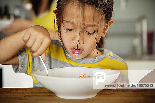 Girl having breakfast at wooden table in kitchen