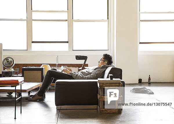 Side view of businessman using laptop while reclining on sofa at office