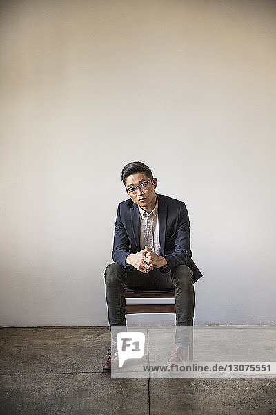 Porträt eines selbstbewussten Geschäftsmannes in voller Länge  der im Büro auf einem Stuhl an der Wand sitzt