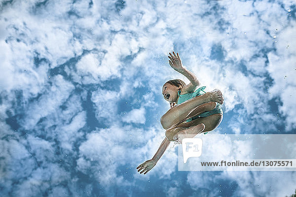 Low angle view of carefree wet girl jumping against cloudy sky