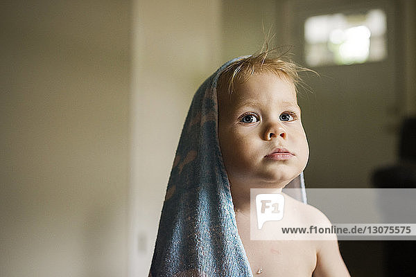 Boy with towel on head looking away while sitting at home