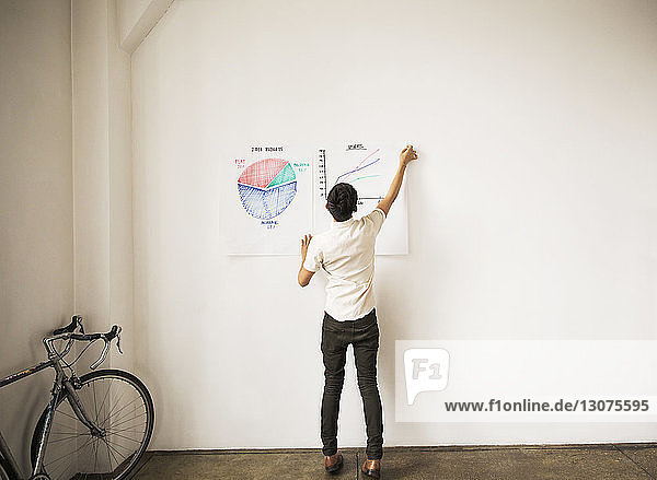Geschäftsmann klebt Grafiken in voller Länge an die weiße Wand im Kreativbüro
