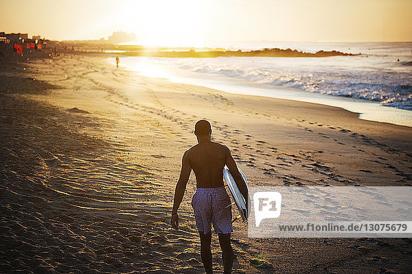 Mann trägt ein Surfbrett  während er am Strand auf Sand läuft