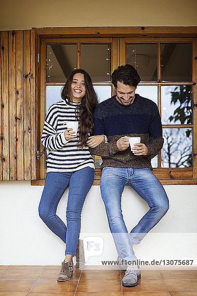Glückliches Paar trinkt Kaffee  während es am Fenster auf der Veranda steht
