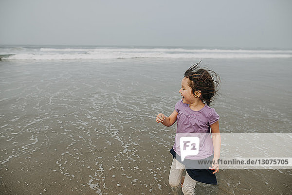 Glückliches Mädchen spielt am Strand gegen den Himmel