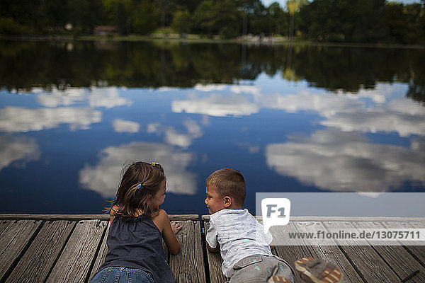 Rear view of siblings relaxing on boardwalk by lake
