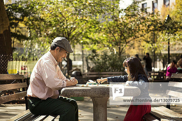 Großvater und Enkelin spielen Brettspiel  während sie im Park am Tisch sitzen